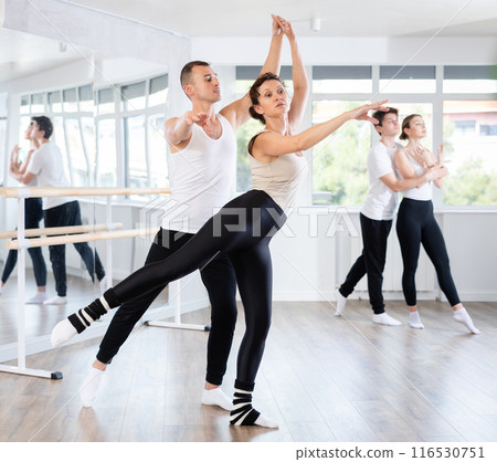 Happy young caucasian man and woman practicing ballet arabesque pose in ballroom Happy young caucasian man and woman practicing ballet arabesque pose in ballroom 116530751