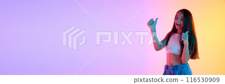 Support and improvement. Happy young girl showing thumbs up with positive smile against gradient pink yellow background in neon light Support and improvement. Happy young girl showing thumbs up with positive smile against gradient pink yellow background in neon light 116530909