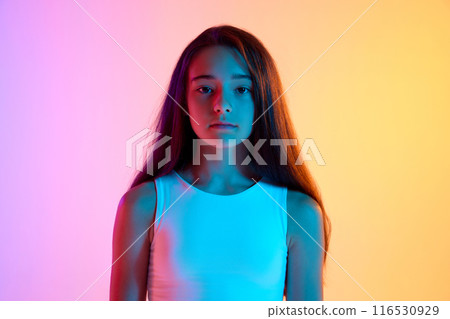 Portrait of beautiful young girl with long brown hair posing with calm expression against gradient pink yellow background in neon light 116530929