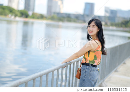 A portrait of happiness pretty young woman in an orange shirt stands near the water, enjoying a sunny day. 116531325
