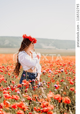 Happy woman in a poppy field in a white shirt and denim skirt with a wreath of poppies on her head posing and enjoying the poppy field. 116532745