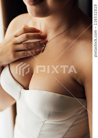 Wedding. Jewelry. The bride in a white dress putting on a necklace around her neck 116532819