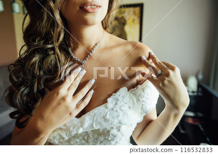 Wedding. Jewelry. The bride in a white dress putting on a necklace around his neck Wedding. Jewelry. The bride in a white dress putting on a necklace around his neck 116532833