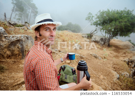 Man sitting outdoors with thermos and cup enjoying nature on a foggy day Man sitting outdoors with thermos and cup enjoying nature on a foggy day 116533054