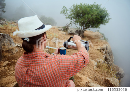 Man in a hat pouring hot drink from thermos on a foggy mountain trail Man in a hat pouring hot drink from thermos on a foggy mountain trail 116533056