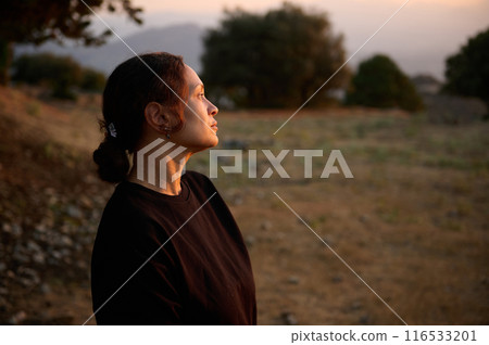Woman admiring sunset in scenic countryside landscape, reflecting and appreciating nature 116533201