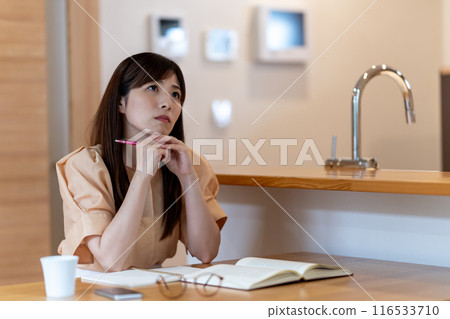A middle-aged woman worried while studying at the dining table 116533710