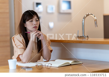 A middle-aged woman worried while studying at the dining table 116533711