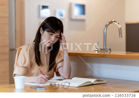 A middle-aged woman worried while studying at the dining table 116533716