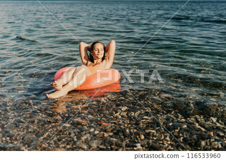 A woman is floating on a red inflatable tube in the ocean A woman is floating on a red inflatable tube in the ocean 116533960