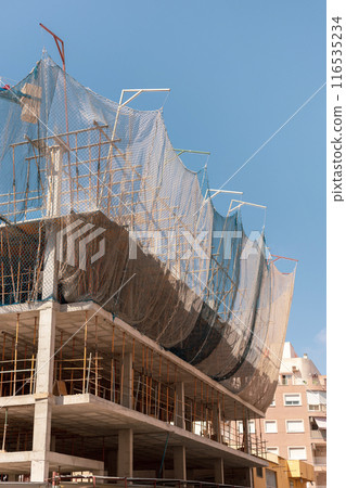 New building construction process. Safety nets and structural beams highlight ongoing work. Detailed shot of multi-level architecture. Ideal for articles on urban development, real estate investment. New building construction process. Safety nets and structural beams highlight ongoing work. Detailed shot of multi-level architecture. Ideal for articles on urban development, real estate investment. 116535234