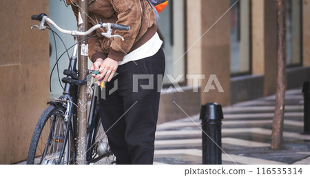 Urban cyclist locking bike to pole, holding keys in hand, amidst city architecture backdrop 116535314