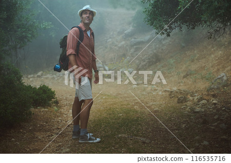 Man hiking in foggy forest path wearing hat and backpack 116535716