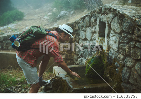 Man refilling water bottle at stone well during a misty mountain hike Man refilling water bottle at stone well during a misty mountain hike 116535755