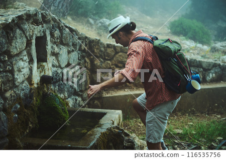 Hiker replenishing water supply at an old stone fountain in a misty forest Hiker replenishing water supply at an old stone fountain in a misty forest 116535756