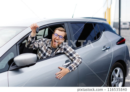 Excited young man showing a car key, sitting inside his new vehicle 116535840