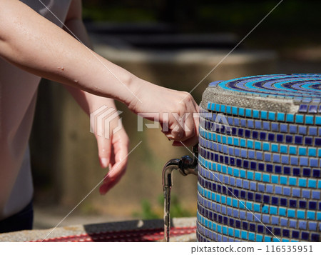Close-up view of a woman's hands and a faucet washing her hands in a summer garden Close-up view of a woman's hands and a faucet washing her hands in a summer garden 116535951