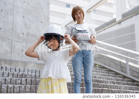 A mother and a girl in elementary school wearing helmets. They participate in disaster prevention training. 116536345