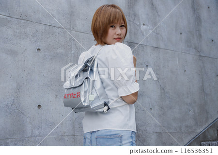 Back view of a woman carrying a disaster prevention backpack. Concrete building background Back view of a woman carrying a disaster prevention backpack. Concrete building background 116536351