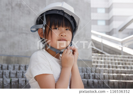 一名戴著白色頭盔的小學生站在一棟混凝土建築的高地上。 116536352