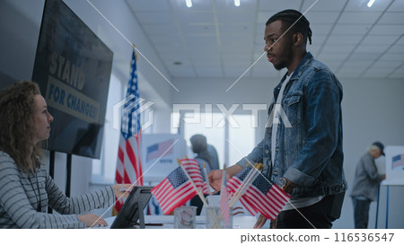 Female polling officer consults male voter, gives ballot for voting Female polling officer consults male voter, gives ballot for voting 116536547