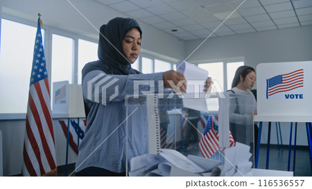 Muslim woman in hijab puts ballot paper in box at polling station 116536557