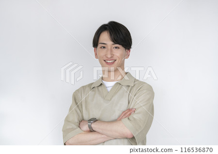 A man in his early 20s smiling while looking at the camera with his arms crossed 116536870