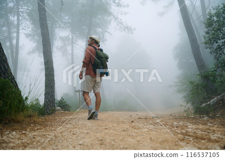 Solo hiker walking through a foggy forest trail with a backpack on a misty morning 116537105
