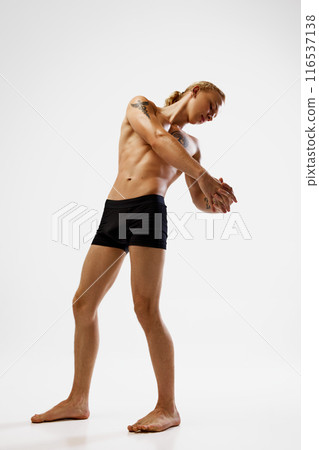 Shirtless man posing in black boxer briefs, his body in dynamic pose with arms extended and hands clasped against white studio background. 116537138