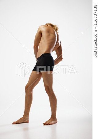 Full length photo of young, shirtless man posing in black underwear showing his muscular body against white studio background. 116537139