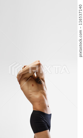 Poster. Wearing black boxer briefs, man poses with his arms hugging his upper body and head leaned back against white studio background. Poster. Wearing black boxer briefs, man poses with his arms hugging his upper body and head leaned back against white studio background. 116537140