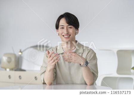 A man in his 20s wearing earphones talking while looking at the camera A man in his 20s wearing earphones talking while looking at the camera 116537173