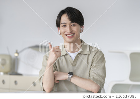 A man in his 20s wearing earphones and looking at the camera making a thumbs up gesture 116537383