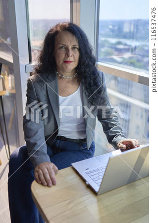 A 57-year-old woman works on a laptop in a modern office workspace 116537476
