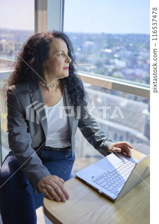 A 57-year-old woman works on a laptop in a modern office workspace 116537478