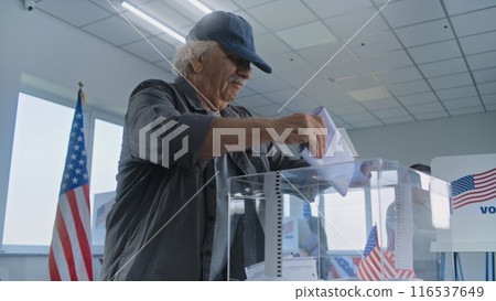 Elderly Caucasian man puts bulletin paper in box at polling station 116537649