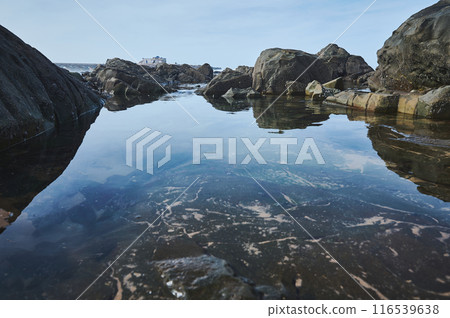 Serene coastal rock pool with clear water reflecting the sky and nearby rocky shore 116539638
