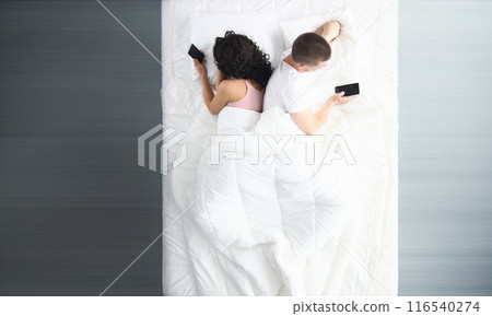 Couple in bed using phones lying backs to each other 116540274