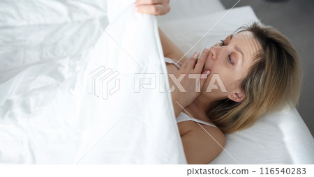 Shocked surprised woman covering face with hand and looking under blanket 116540283