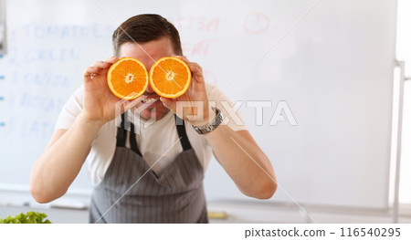 Man holding cut oranges at eye level instead of glasses Man holding cut oranges at eye level instead of glasses 116540295