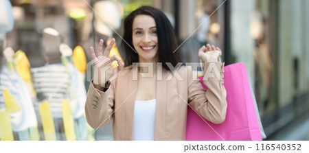 Happy smiling woman with shopping bags showing ok gesture 116540352