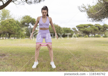 A Young Woman Is Strengthening Her Muscles by Exercising With a Resistance Band in the Park A Young Woman Is Strengthening Her Muscles by Exercising With a Resistance Band in the Park 116540742