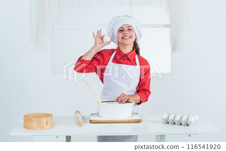 one more egg. making cake by recipe. time to eat. happy child cooking in kitchen. bake cookies in kitchen. professional and skilled baker. kid in chef uniform and hat. teen girl preparing dough 116541920