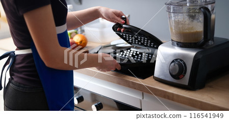 Woman preparing belgian waffle maker in kitchen Woman preparing belgian waffle maker in kitchen 116541949