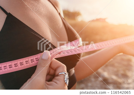 A woman is holding a pink tape measure and is measuring her breasts after morning fitness 116542065