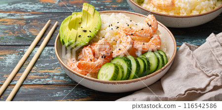 White ceramic bowl with rice, shrimps, avocado, vegetables and sesame seeds and chopsticks on colourful rustic wooden background front view. Healthy asian style poke bowl 116542586