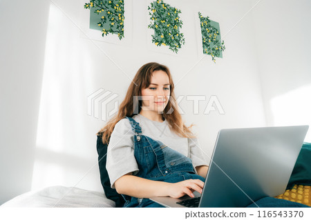 Female student watching video online webinar learn on laptop sitting on the bed with tea cup distance e-learning course video conference pc call in bedroom at home. Work from home, freelance concept. 116543370