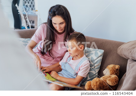 Young Mother and her preschooler son on the sofa reading book for children at home. Studying and playing together at home. Happy childhood and motherhood concept. Selective focus. 116543404