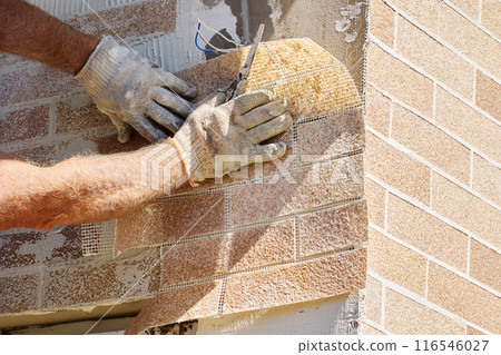 Acrylic marble chips as part of flexible faux brick panels that construction worker glues to facade of house. 116546027