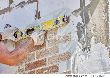 Spirit level is used for determining horizontal level of faux brick panel glued to wall of building faade. 116546030